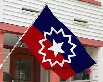 Könnte beinhalten: Eine Flagge mit rotem und blauem Design, mit einem weißen Stern in einem weißen, 13-zackigen Stern. Die Flagge ist an einer Stange befestigt und vor einem weißen Haus mit rotem Zierrat ausgestellt.