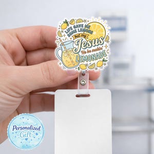 May include: A badge reel featuring a clear acrylic topper with a colorful illustration of a pitcher of lemonade, lemon slices, and flowers. The text reads: Life gave me some lemons but my Jesus He be makin' lemonade in blue and brown lettering.