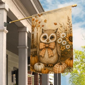 May include: A rectangular garden flag featuring a brown owl with a large orange and white plaid bow tie. The owl is surrounded by orange and white pumpkins, white daisies, and yellow sunflowers against a rustic wooden fence background.