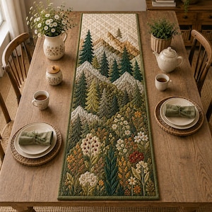 May include: A rectangular quilted table runner featuring a landscape design with embroidered mountains, evergreen trees, and a foreground of colorful wildflowers in shades of green, yellow, orange, and white, finished with a dark green border.
