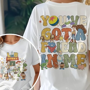 Op de afbeelding: Wit T-shirt met een kleurrijke afbeelding van personages en tekst uit de film "Toy Story". De tekst op de achterkant luidt "You've Got a Friend in Me". De voorkant van het shirt heeft de tekst "Lab Story".