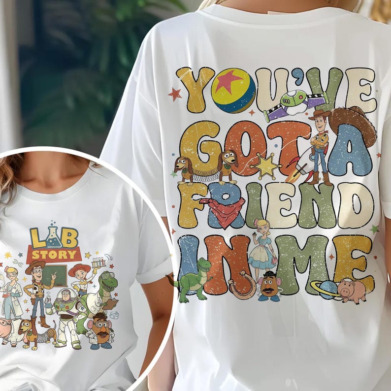 Op de afbeelding: Wit T-shirt met een kleurrijke afbeelding van personages en tekst uit de film "Toy Story". De tekst op de achterkant luidt "You've Got a Friend in Me". De voorkant van het shirt heeft de tekst "Lab Story".