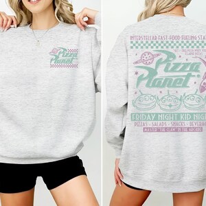 May include: Light gray sweatshirt with "Pizza Planet" logo on the front and back. The back features the text "Interstellar Fast-Food Fueling Station" and "Friday Night Kid Night" with alien graphics and other text.