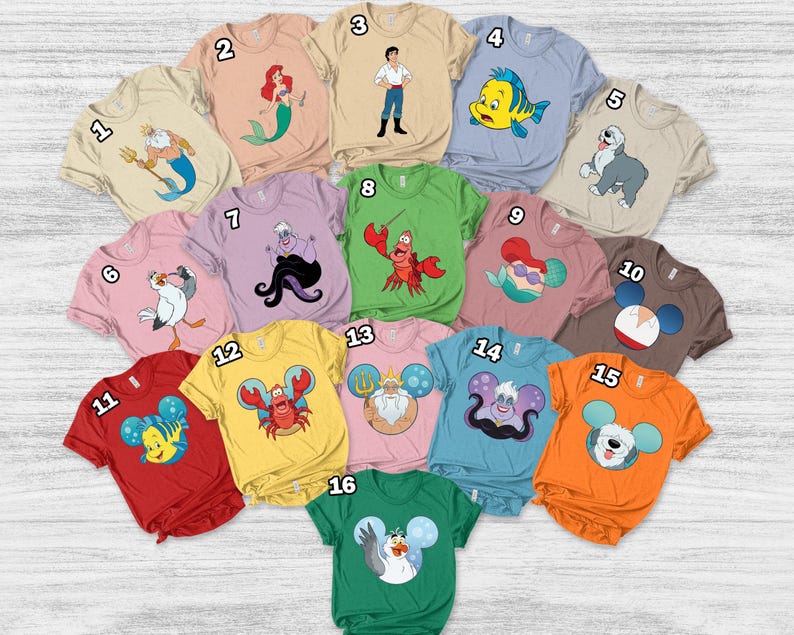 May include: A collection of short-sleeved t-shirts in various colors, each featuring a cartoon character design. Designs include a mermaid, a crab, and a dog. The shirts are arranged on a light wood surface.
