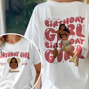 May include: White t-shirt featuring a graphic of a cartoon character holding a wooden paddle, with the words "Birthday Girl" in red. The shirt also includes the character's name and the year 2021.