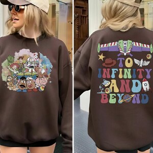 May include: A brown sweatshirt featuring a colorful graphic of characters from a popular animated movie on the front. The back of the sweatshirt has the phrase "TO INFINITY AND BEYOND" with related imagery. The sweatshirt is a casual style.