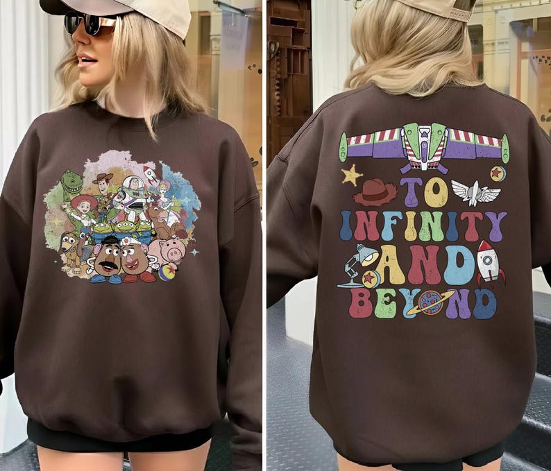 May include: A brown sweatshirt featuring a colorful graphic of characters from a popular animated movie on the front. The back of the sweatshirt has the phrase "TO INFINITY AND BEYOND" with related imagery. The sweatshirt is a casual style.