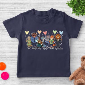 May include: Navy blue toddler t-shirt featuring a colorful graphic of characters from Zootopia, each holding a balloon. The characters include Flash, Chief Bogo, Gary, Judy Hopps, Nick Wilde, and Mayor Lionheart. The names of the characters are printed below them.