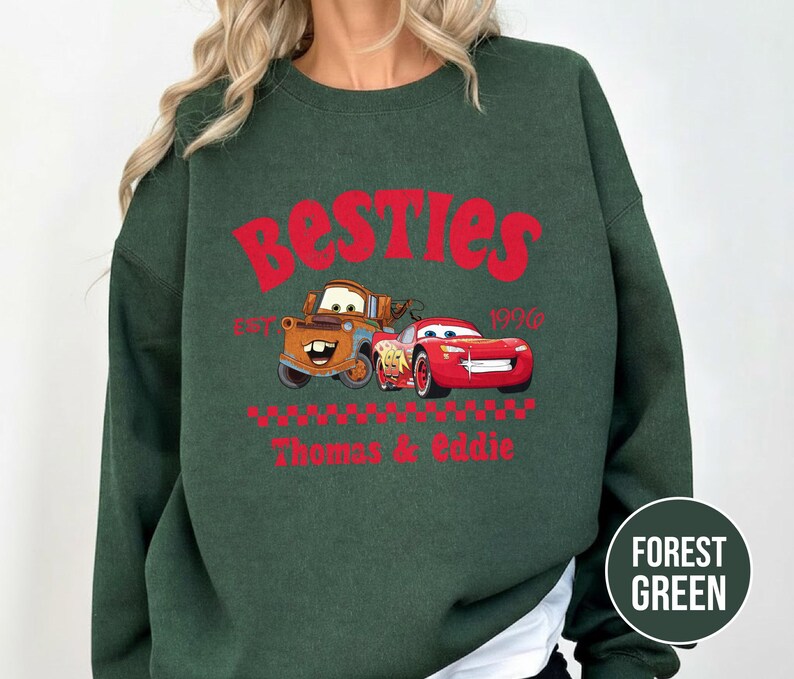 May include: Forest green sweatshirt featuring the word "Besties" in red, with cartoon car graphics. The design includes the text "Est. 1996" and the names "Thomas & Eddie" in red.