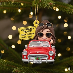May include: A Christmas ornament featuring a figurine of a person driving a red vintage car. The figurine has sunglasses and a learner's permit that reads "Gillian, 2025." The car's license plate says "Look out world, here I come!"