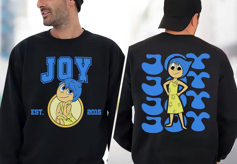 May include: Black sweatshirt featuring the word "JOY" in blue block letters with a cartoon character illustration. The back of the sweatshirt has the word "JOY" repeated in a pattern with the same character.