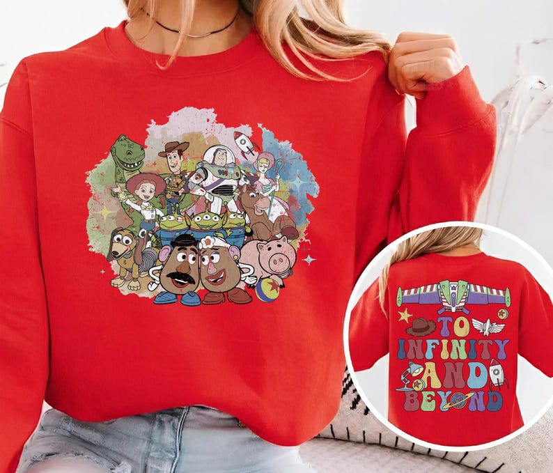 May include: A red sweatshirt featuring a colorful graphic of characters from the animated film "Toy Story." The front of the sweatshirt displays a group of characters, while the back has the phrase "To Infinity and Beyond."
