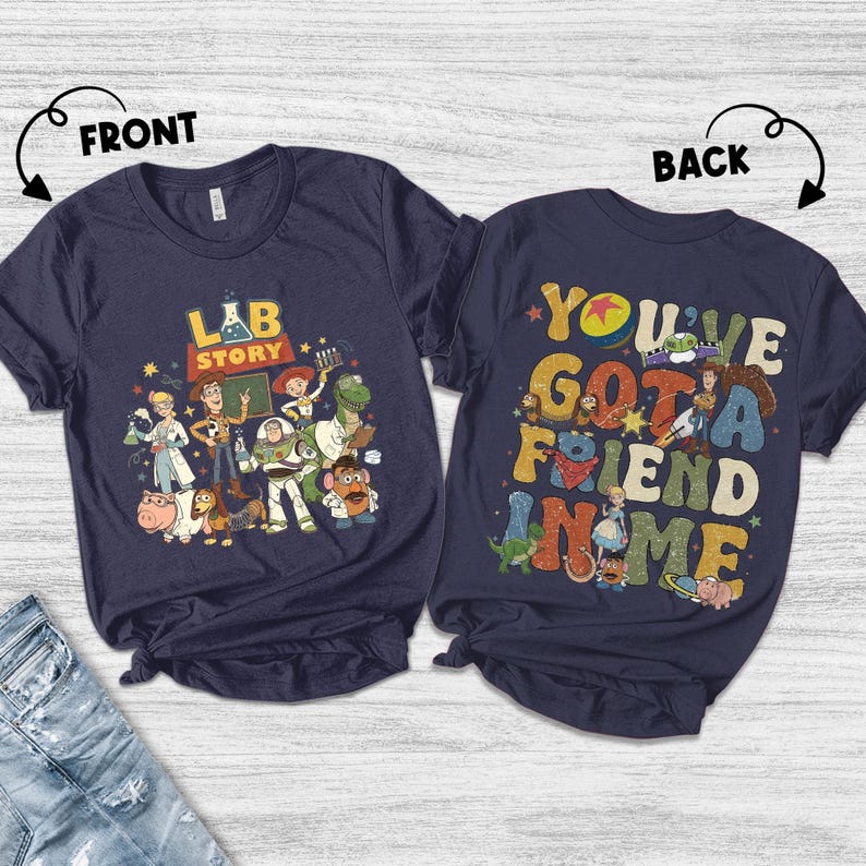 Op de afbeelding: Twee marineblauwe t-shirts met kleurrijke graphics. Het shirt aan de voorkant heeft de tekst "LAB STORY" met cartoonfiguren. Het shirt aan de achterkant zegt "YOU'VE GOT A FRIEND IN ME" met meer cartoonfiguren. Beide shirts zijn korte mouwen.
