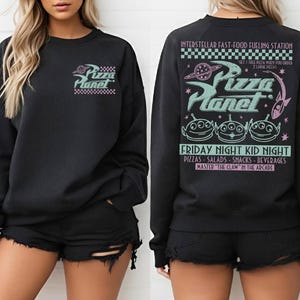 May include: Black sweatshirt with a Pizza Planet graphic on the front and back. The front features the logo, while the back displays the text "INTERSTELLAR FAST-FOOD FUELING STATION" and "FRIDAY NIGHT KID NIGHT" with alien characters.
