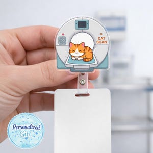 May include: A badge reel featuring a cartoon cat inside a CAT SCAN machine. The cat is orange and white, and the machine is light blue and white. The badge reel has a clear plastic strap and a white rectangular area for a name tag.
