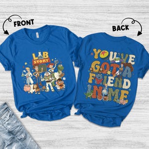 Op de afbeelding: Twee blauwe T-shirts met Toy Story-graphics. Het shirt aan de voorkant heeft de tekst "LAB STORY" met karakterillustraties. Het shirt aan de achterkant zegt "YOU'VE GOT A FRIEND IN ME" met karakterillustraties. Beide shirts zijn korte mouwen.