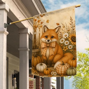 May include: A decorative garden flag featuring a central illustration of a fox wearing a plaid bow tie, surrounded by autumn pumpkins, white daisies, and sunflowers. The scene is set against a light beige background with a wooden fence and leaves.