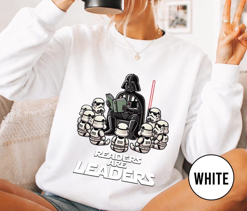 K&ouml;nnte beinhalten: Wei&szlig;es Sweatshirt mit einer Cartoon-Illustration von Darth Vader, der einer Gruppe von Sturmtruppen vorliest. Der Text "Readers are Leaders" ist unter der Illustration aufgedruckt. Ein rotes Lichtschwert ist ebenfalls zu sehen.