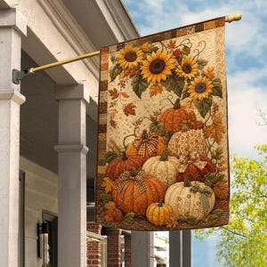 May include: A vertical garden flag featuring a quilted-style print of sunflowers and various pumpkins in shades of orange, cream, and brown. The design includes autumn leaves and vines, with a checkered border, hanging from a gold metal pole.