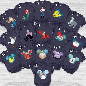May include: A collection of navy blue t-shirts featuring various characters from a popular animated film. The designs include a mermaid, a crab, a fish, and other characters. The shirts are arranged on a light gray surface.