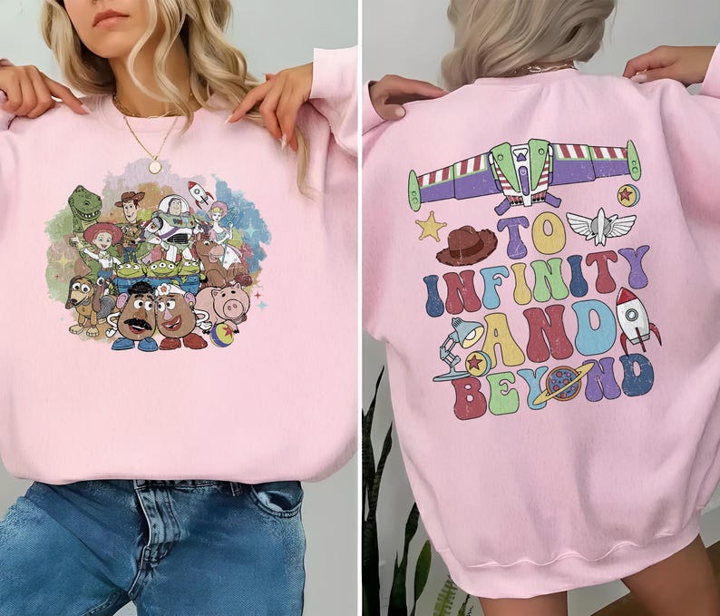 May include: A light pink sweatshirt featuring a colorful graphic of Toy Story characters on the front. The back of the sweatshirt has a graphic of Buzz Lightyear's ship and the phrase "To Infinity and Beyond" in a retro font.