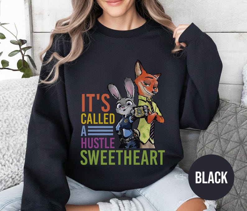 Puede incluir: Sudadera negra con un gr&aacute;fico colorido de Judy Hopps y Nick Wilde de Zootopia, con el texto "IT'S CALLED A HUSTLE SWEETHEART". La sudadera tiene cuello redondo y mangas largas.