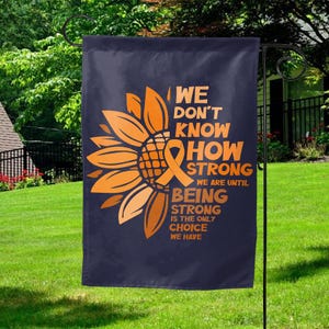 May include: A dark blue garden flag featuring a large orange sunflower with an orange awareness ribbon at its center. The text reads: WE DON'T KNOW HOW STRONG WE ARE UNTIL BEING STRONG IS THE ONLY CHOICE WE HAVE in bold orange capital letters.