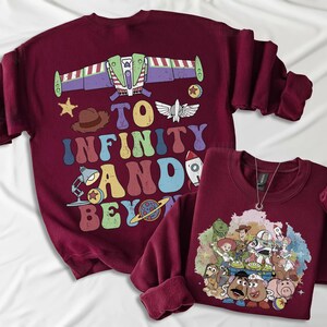 May include: Two maroon sweatshirts. One features a graphic of Buzz Lightyear's spaceship and the phrase "To Infinity and Beyond" in colorful letters. The other has a graphic of Toy Story characters. Both have long sleeves.