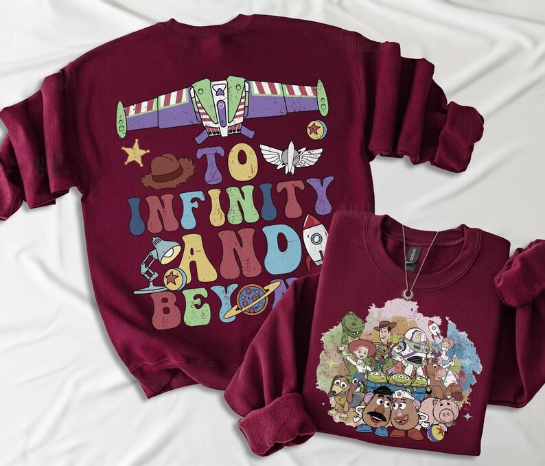 May include: Two maroon sweatshirts. One features a graphic of Buzz Lightyear's spaceship and the phrase "To Infinity and Beyond" in colorful letters. The other has a graphic of Toy Story characters. Both have long sleeves.