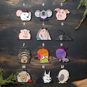 May include: A collection of twelve cartoon character face cutouts, each with a unique design. The characters include a mouse, koala, pig, elephant, gorilla, porcupine, frog, camel, lion, wolf, and sheep. The cutouts are arranged on a dark wooden surface.