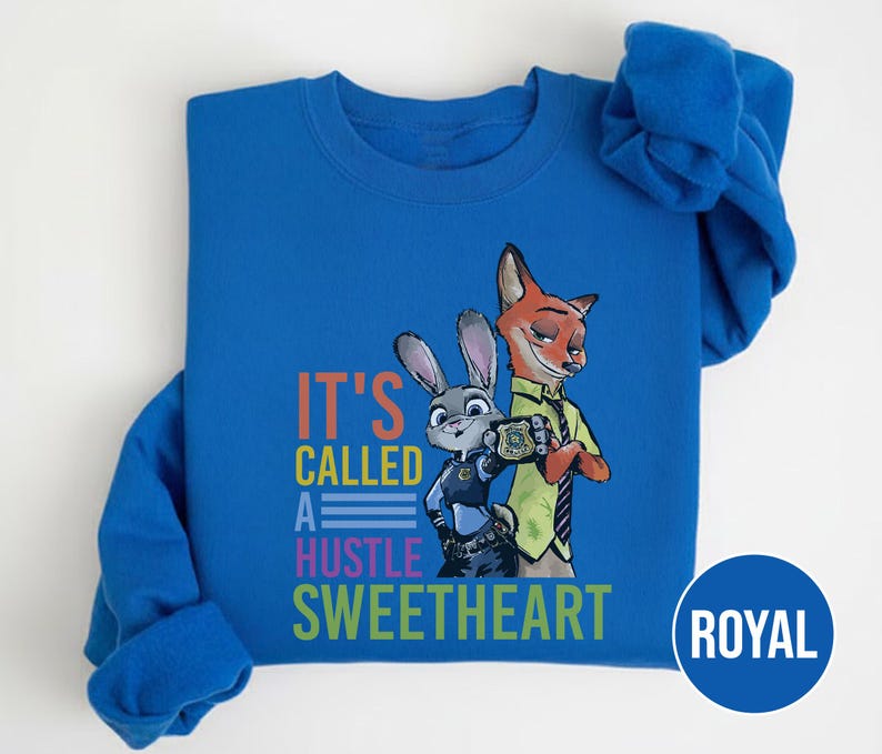 Puede incluir: Sudadera azul real con un gr&aacute;fico de un zorro y un conejo con uniformes de polic&iacute;a. El texto "IT'S CALLED A HUSTLE SWEETHEART" est&aacute; impreso en naranja, azul y verde. La sudadera tiene mangas largas y cuello redondo.