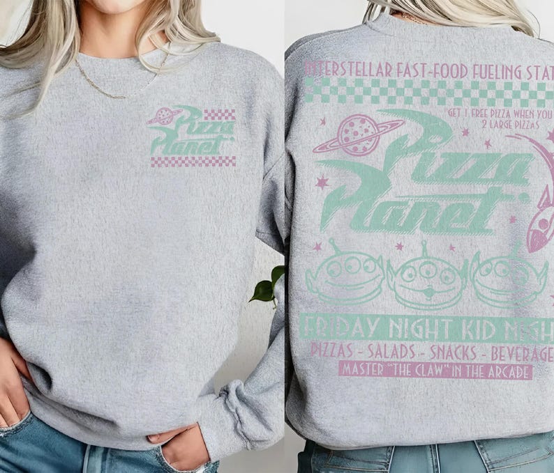 May include: A light gray sweatshirt featuring the Pizza Planet logo in mint and pink. The back of the sweatshirt has the text "Interstellar Fast-Food Fueling Station" and "Friday Night Kid Nite" with alien graphics.