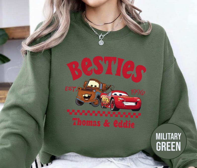 May include: Military green sweatshirt featuring the text "Besties" in red, with cartoon images of Mater and Lightning McQueen. The sweatshirt also includes the text "Est. 1996" and "Thomas & Eddie".