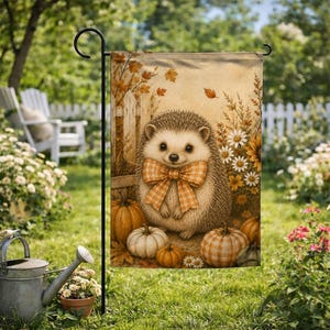 May include: A rectangular garden flag featuring a central illustration of a hedgehog wearing an orange and white plaid bow tie. The hedgehog is surrounded by pumpkins, white daisies, and autumn leaves against a wooden fence background.