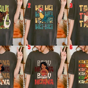 May include: Dark gray t-shirts featuring characters and text from a popular animated film. Designs include Maui, Hei Hei, Tala, Moana, Baby Moana, and the Kakamora. Each shirt has a unique graphic and text.