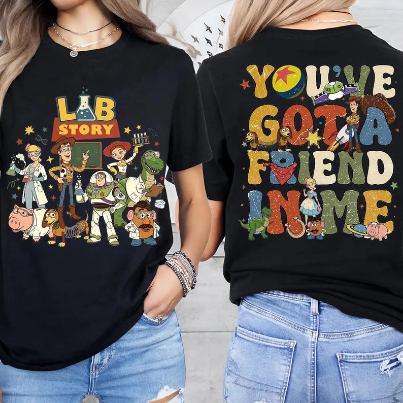 Op de afbeelding: Zwarte t-shirts met kleurrijke afbeeldingen. E&eacute;n shirt heeft de tekst "LAB STORY" met cartoonfiguren. Het andere shirt toont "YOU'VE GOT A FRIEND IN ME" met meer cartoonfiguren. Beide shirts hebben een vintage stijl.