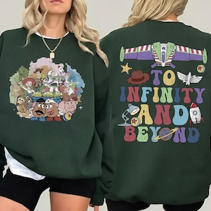 May include: Dark green sweatshirt featuring a colorful graphic of Toy Story characters on the front. The back of the sweatshirt has the phrase "To Infinity and Beyond" with a Buzz Lightyear spaceship design and other themed graphics.