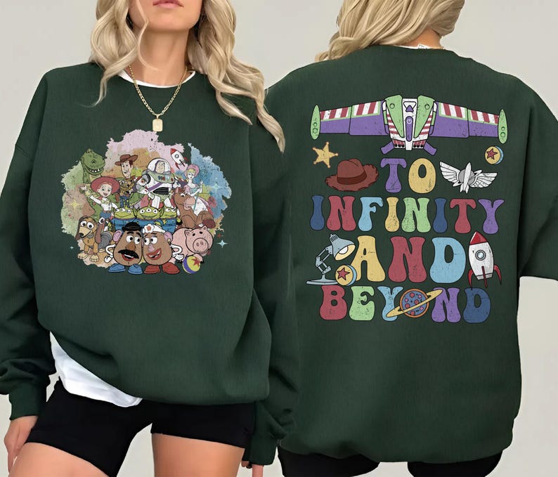 May include: Dark green sweatshirt featuring a colorful graphic of Toy Story characters on the front. The back of the sweatshirt has the phrase "To Infinity and Beyond" with a Buzz Lightyear spaceship design and other themed graphics.