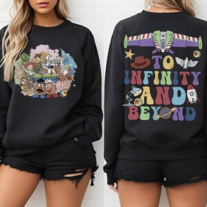May include: Black sweatshirt featuring a colorful graphic of characters from a popular animated movie on the front. The back of the sweatshirt displays the text "TO INFINITY AND BEYOND" with related imagery. A fun and nostalgic apparel item.