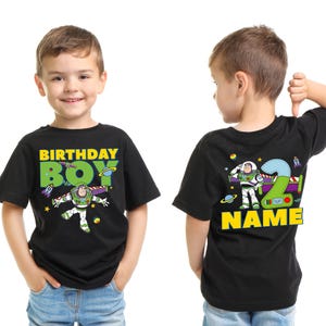 Pu&ograve; includere: T-shirt nera con grafica di Buzz Lightyear e la scritta "BIRTHDAY BOY" in giallo e verde. Il retro della maglietta presenta un grande numero "2" e la parola "NAME" in giallo. La maglietta &egrave; indossata da un bambino.