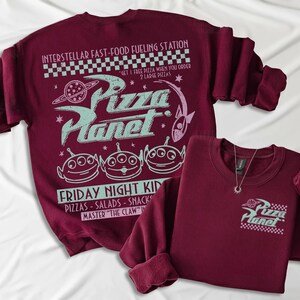 May include: Two maroon sweatshirts with the Pizza Planet logo and graphics. One sweatshirt has a large design on the back with the text "Interstellar Fast-Food Fueling Station" and "Friday Night Kid". The other has a small logo on the front.