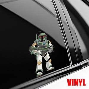 Puede incluir: Una calcoman&iacute;a de vinilo con una ilustraci&oacute;n de dibujos animados de un personaje con una armadura verde y blanca, sosteniendo un rifle. El personaje est&aacute; sobre una superficie negra, con la palabra "VINYL" en rojo en la parte inferior.