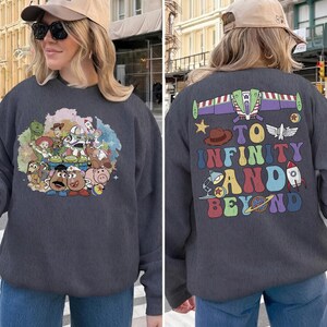 May include: Dark gray sweatshirt featuring a colorful graphic of Toy Story characters on the front. The back of the sweatshirt displays the phrase "To Infinity and Beyond" with related imagery. A casual, comfortable garment.