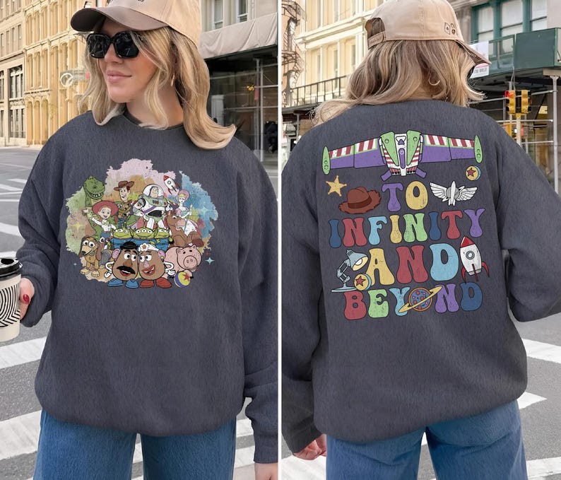 May include: Dark gray sweatshirt featuring a colorful graphic of Toy Story characters on the front. The back of the sweatshirt displays the phrase "To Infinity and Beyond" with related imagery. A casual, comfortable garment.