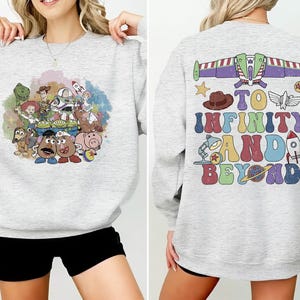 May include: Light gray sweatshirt featuring a colorful graphic of Toy Story characters on the front. The back of the sweatshirt has the phrase "To Infinity and Beyond" with related imagery. A fun and comfortable top for fans of the animated film.