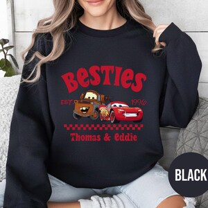 May include: Black sweatshirt featuring the text "Besties" in red, with the year "1996" and the names "Thomas & Eddie" below. The design includes cartoon images of two cars. A black circle with the word "BLACK" is at the bottom.