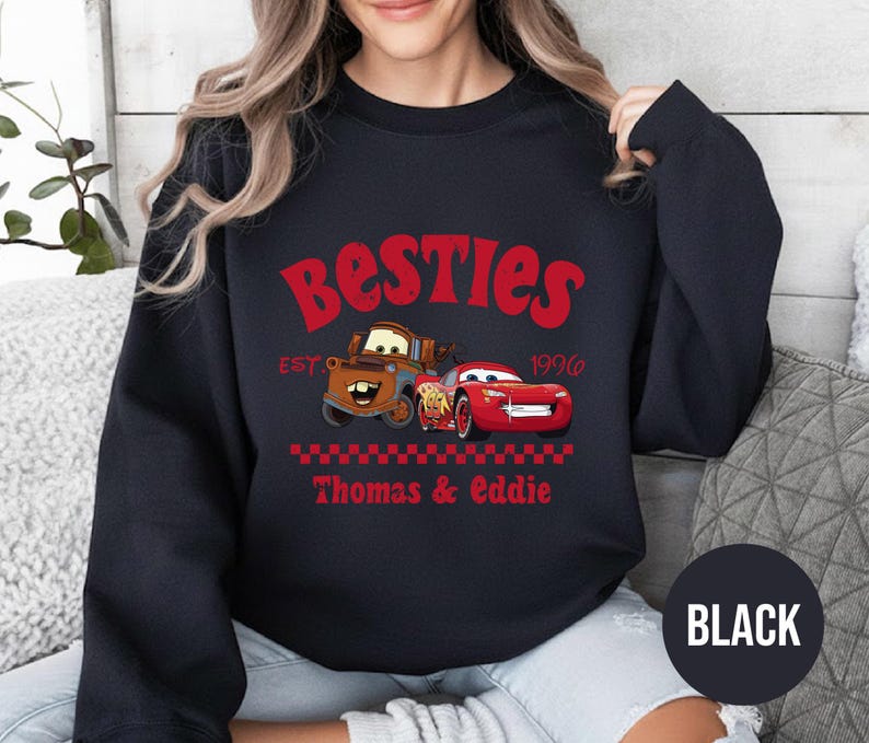 May include: Black sweatshirt featuring the text "Besties" in red, with the year "1996" and the names "Thomas & Eddie" below. The design includes cartoon images of two cars. A black circle with the word "BLACK" is at the bottom.