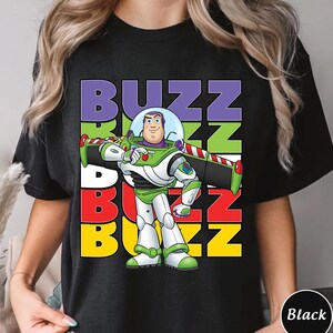 Puede incluir: Camiseta negra con un dise&ntilde;o colorido de Buzz Lightyear de Toy Story. El dise&ntilde;o incluye la palabra "BUZZ" en letras apiladas y coloridas. Buzz Lightyear se muestra con su traje de guardi&aacute;n espacial.