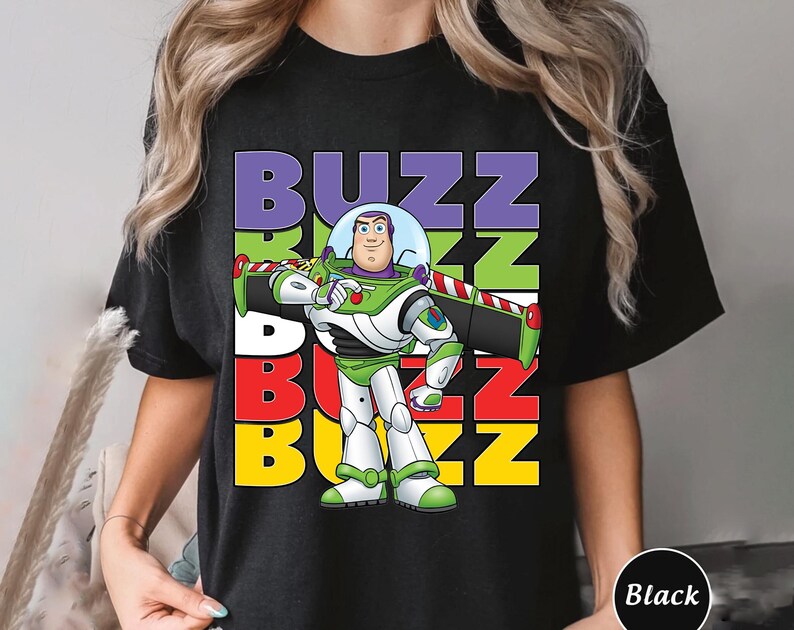 Puede incluir: Camiseta negra con un dise&ntilde;o colorido de Buzz Lightyear de Toy Story. El dise&ntilde;o incluye la palabra "BUZZ" en letras apiladas y coloridas. Buzz Lightyear se muestra con su traje de guardi&aacute;n espacial.