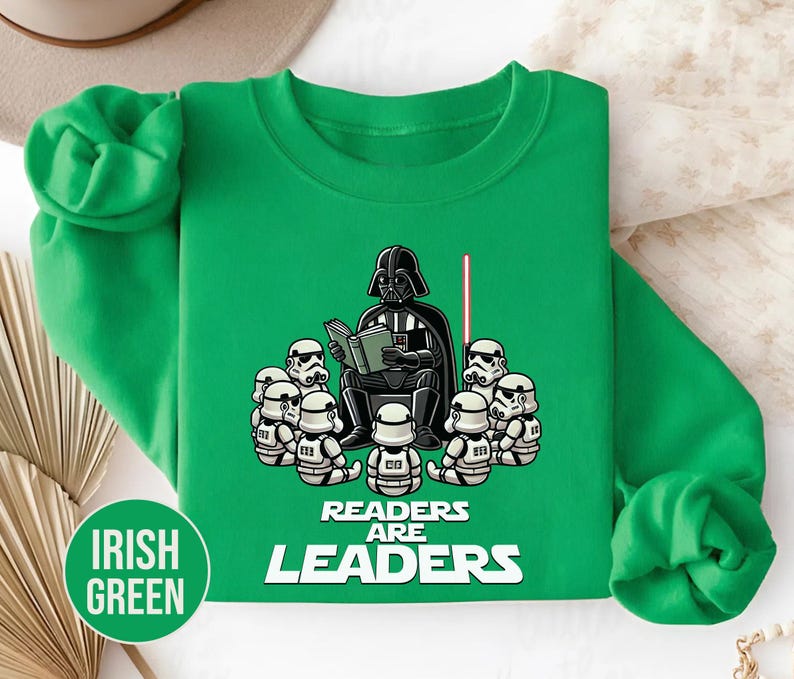 K&ouml;nnte beinhalten: Irisch gr&uuml;nes Sweatshirt mit einer Cartoon-Illustration von Darth Vader, der Stormtroopern vorliest. Der Text "READERS ARE LEADERS" befindet sich darunter. Ein rotes Lichtschwert ist ebenfalls zu sehen.